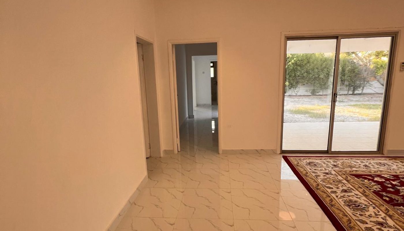 Interior view of a room with white marble-tiled floor, beige walls, a large rug, sliding glass doors, and doorways leading to other rooms.