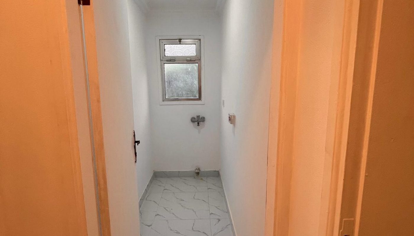 A small, empty room with white walls, a tiled floor, a window, and plumbing fixtures, likely intended for use as a bathroom or utility space.