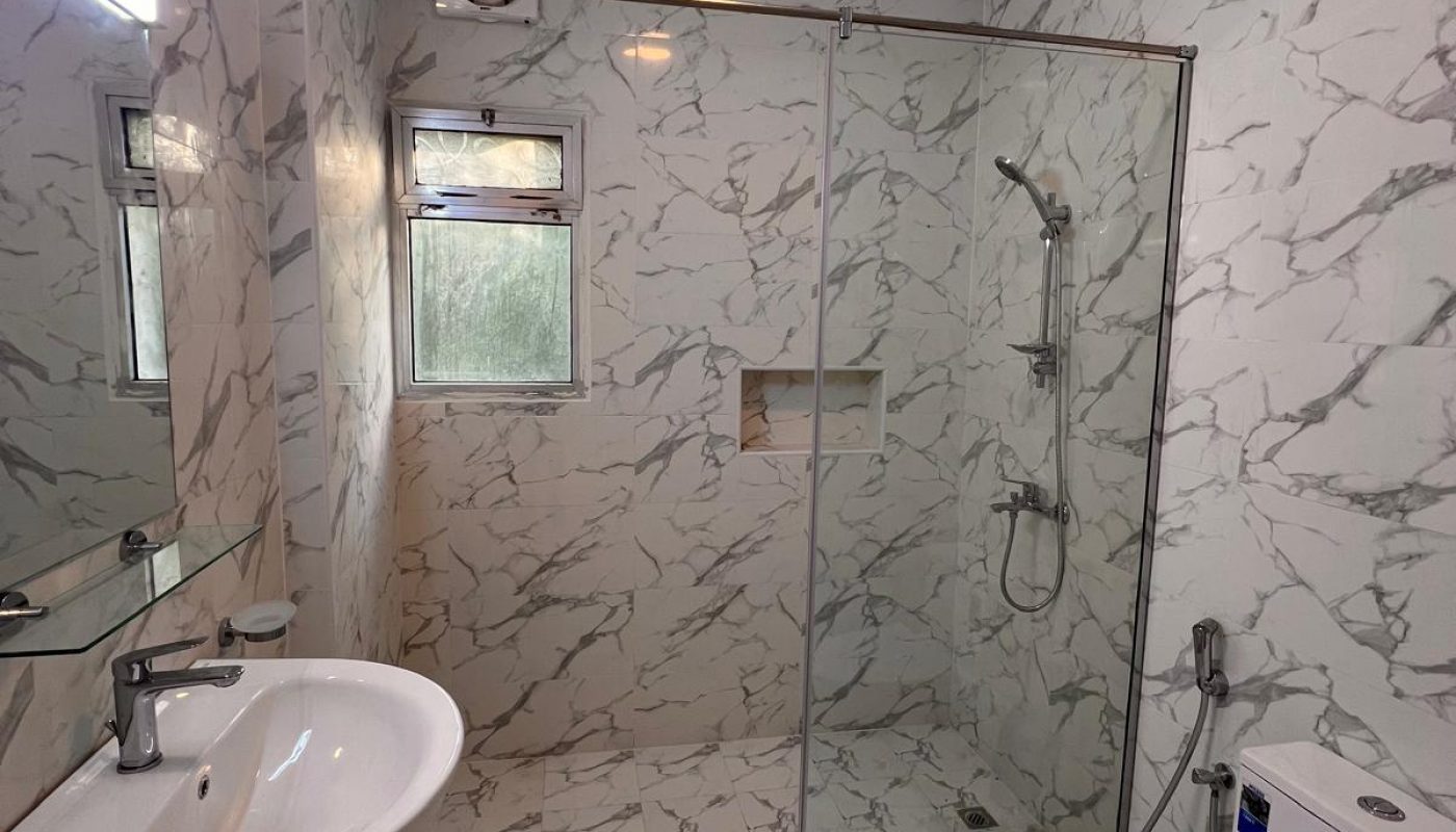 Modern bathroom with marble-patterned walls and floor, a wall-mounted sink, toilet, and a walk-in glass shower enclosure with a rainfall showerhead.