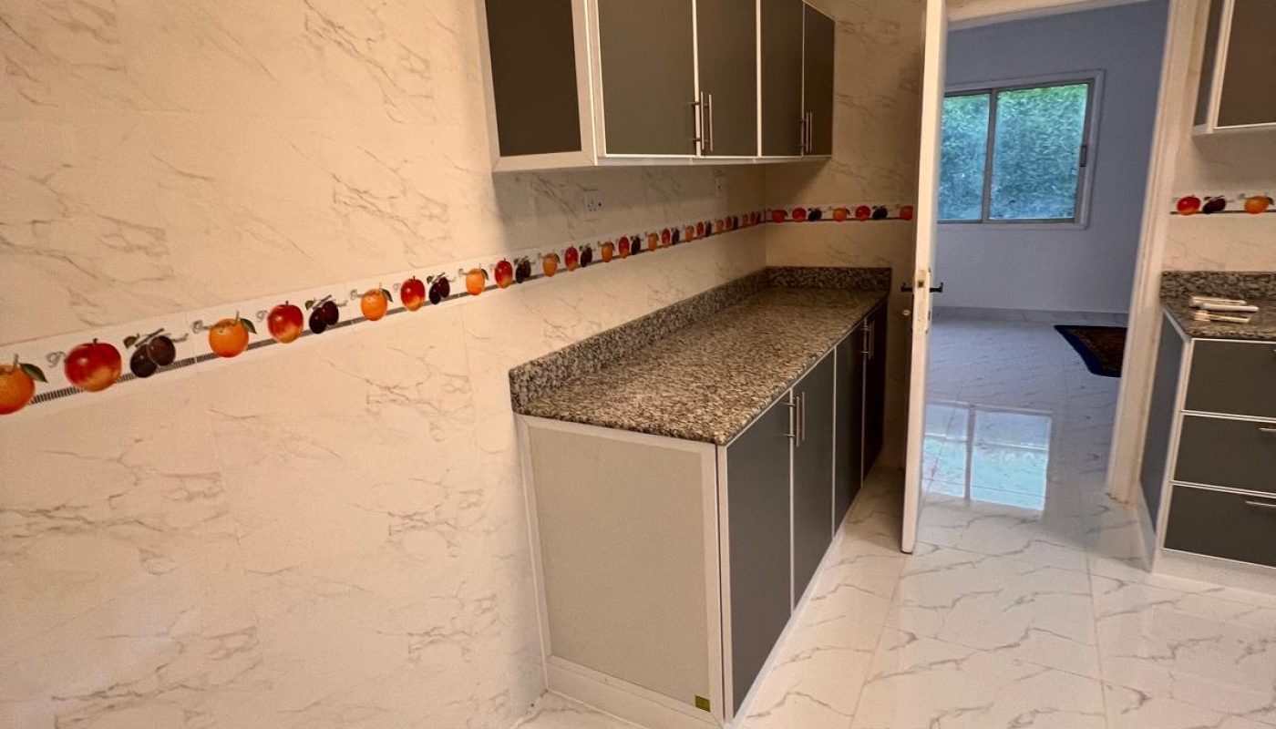 A modern kitchen with marble-patterned walls and floors, gray cabinets, granite countertops, and a fruit-themed border tile along the wall.