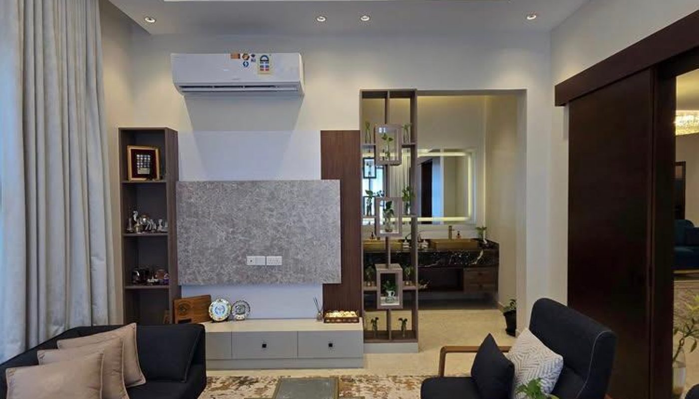 Modern living room with dark sofas, a marble coffee table, decorative shelves, a chandelier, and air conditioning, featuring neutral tones and contemporary decor.
