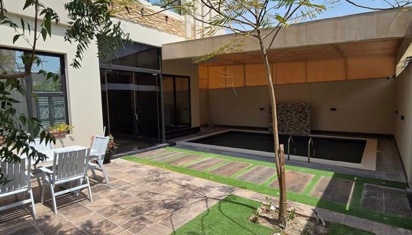 Modern courtyard with artificial grass, tiled patio, small pool, and white outdoor dining set under clear blue sky.