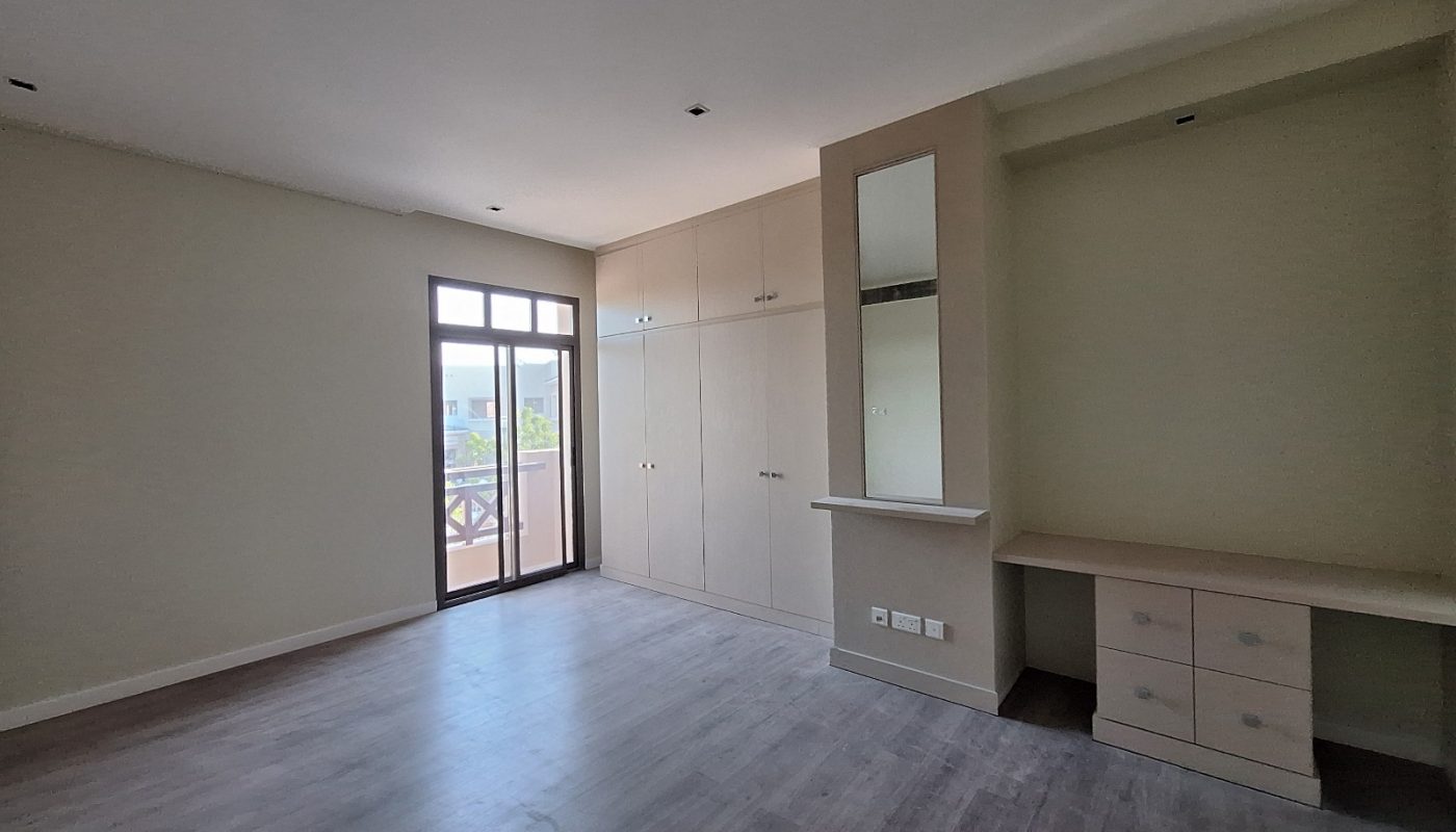 Empty room with wooden flooring, built-in wardrobes, a dressing table with mirror, and a glass door leading to a balcony.