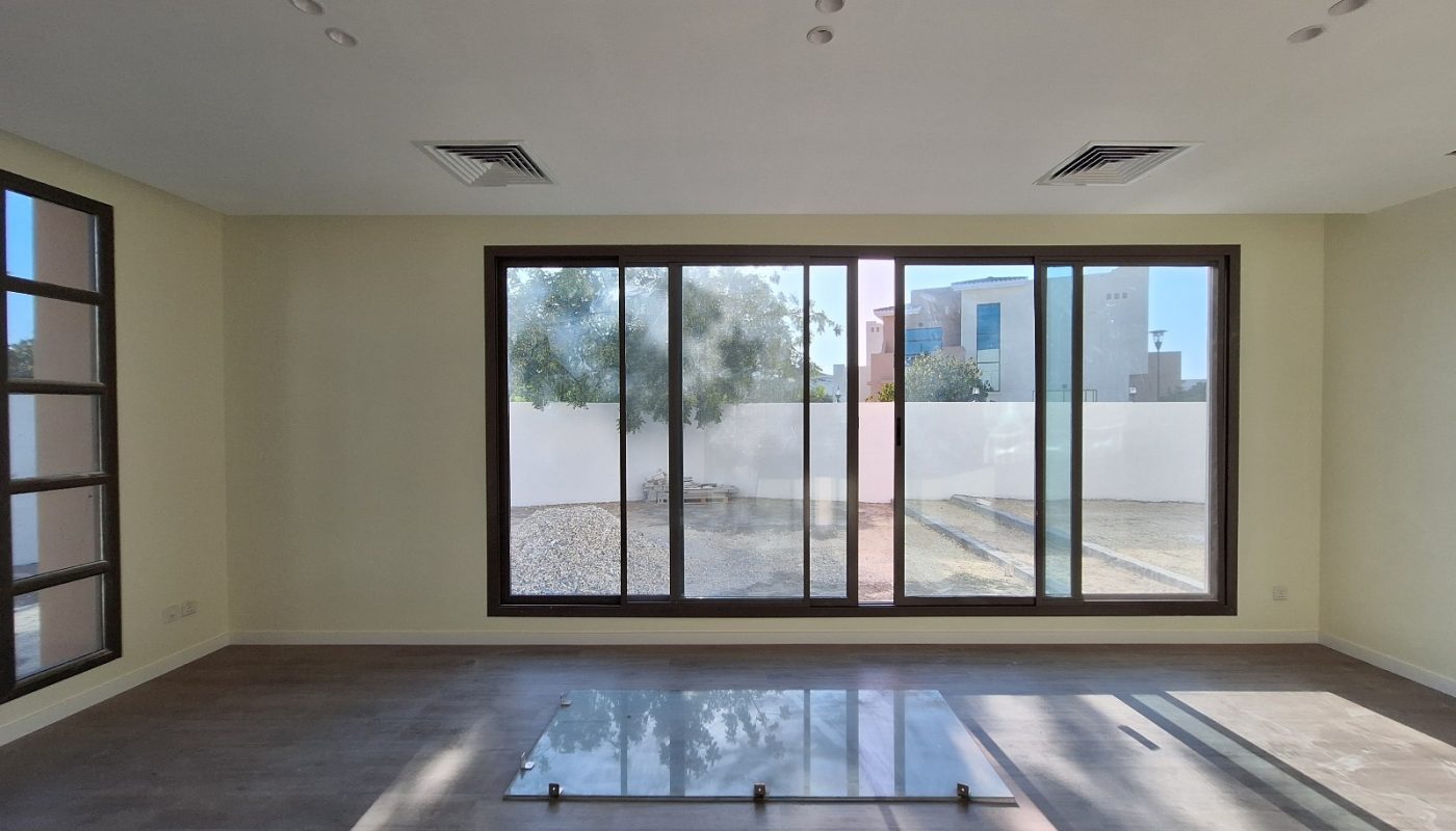 An empty room with large sliding glass doors leading to a backyard, wooden floors, and a glass panel resting on the floor.