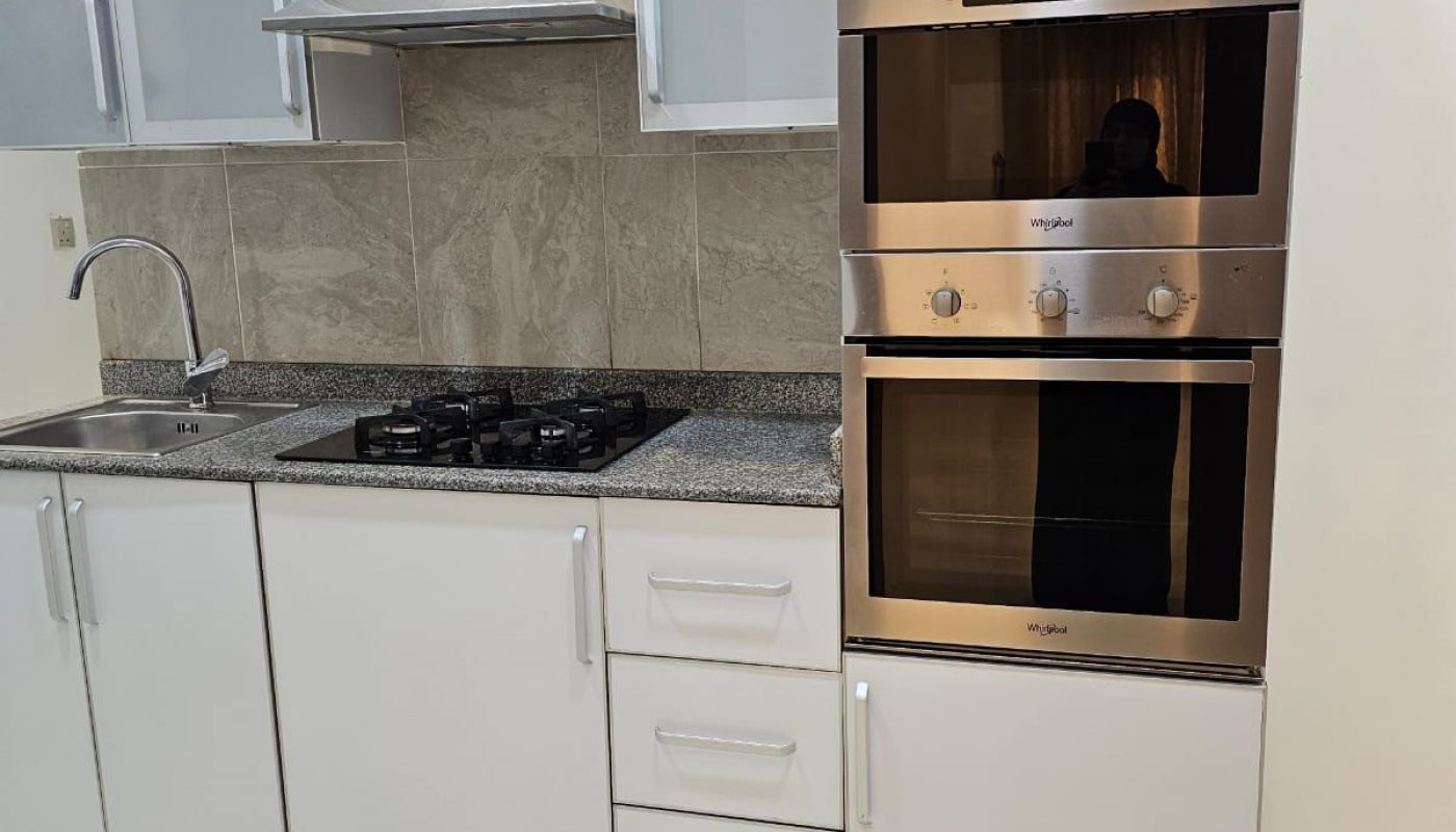 Modern kitchen with white cabinets, stainless steel oven and stove, overhead range hood, granite countertop, and tiled backsplash.