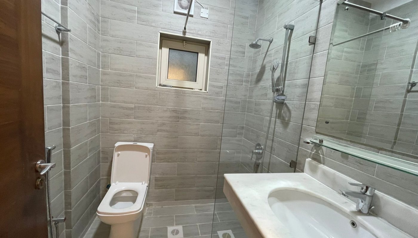 A modern bathroom with a wall-mounted toilet, a glass-enclosed shower area, a rectangular sink, and a small window above the toilet.