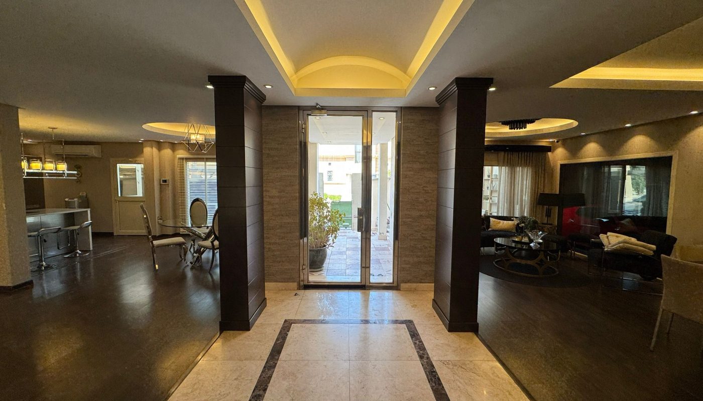 Spacious modern home interior with marble hallway, dark wood floors, and glass doors leading outside; open dining and living areas on either side.