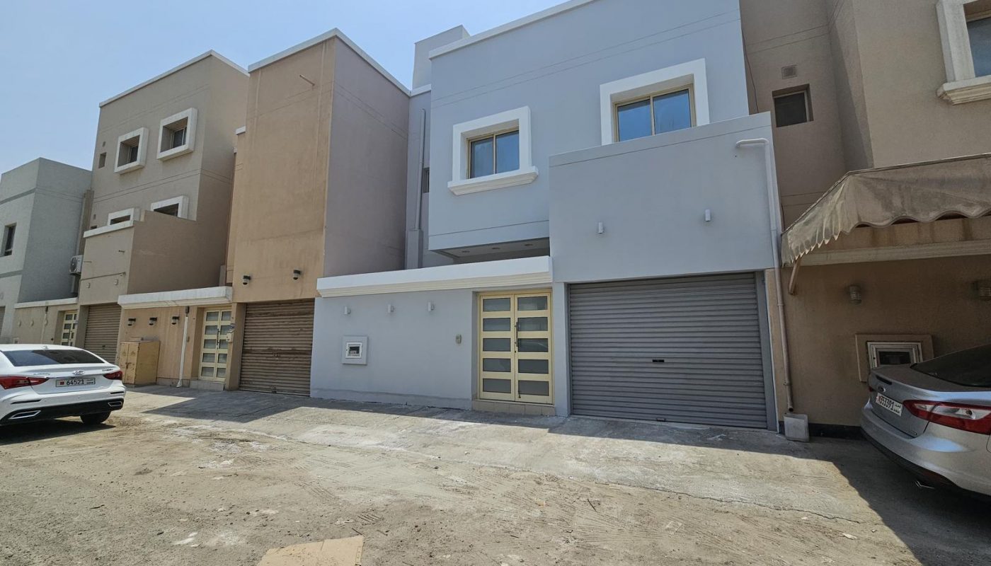 A row of modern, two-story townhouses with garages and parked cars on a sunny day.