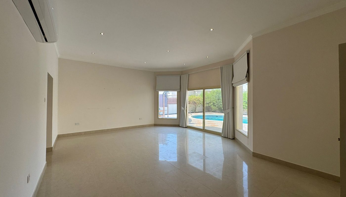 Unfurnished, spacious living room with tiled floor, large windows with blinds, and a view of a swimming pool and trees outside. Ceiling lights and air conditioning unit visible.