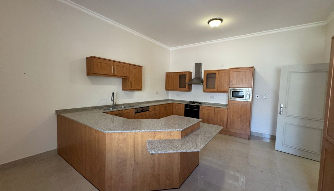 Modern kitchen with wood cabinets, granite countertops, an island with a raised bar, built-in oven, stovetop, microwave, and light beige tile flooring.