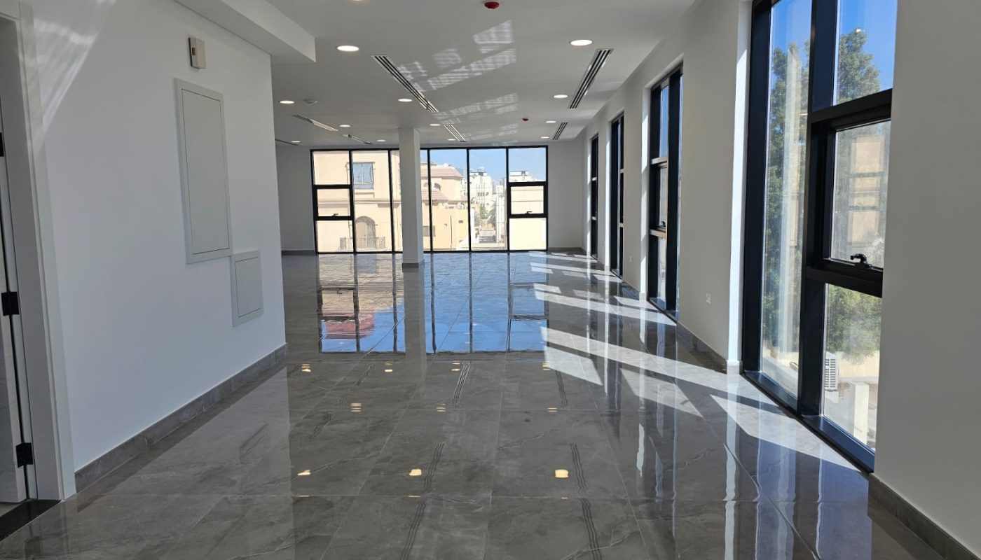 A modern, empty corridor with large windows on one side, glossy tiled floors, and natural light streaming in.