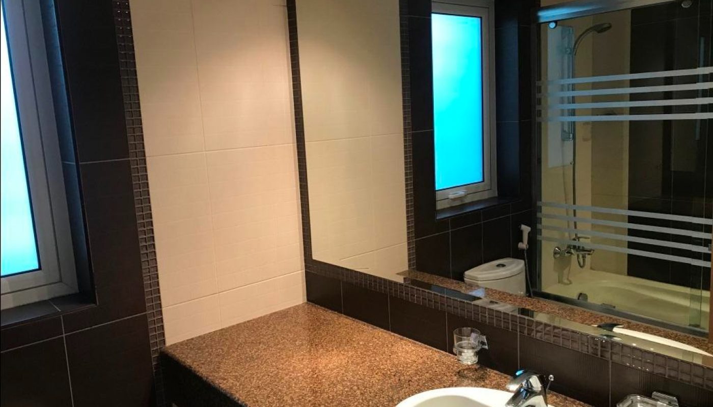 Modern bathroom with a brown countertop, white sink, large mirror, frosted windows, and a glass-enclosed bathtub with horizontal frosted stripes.