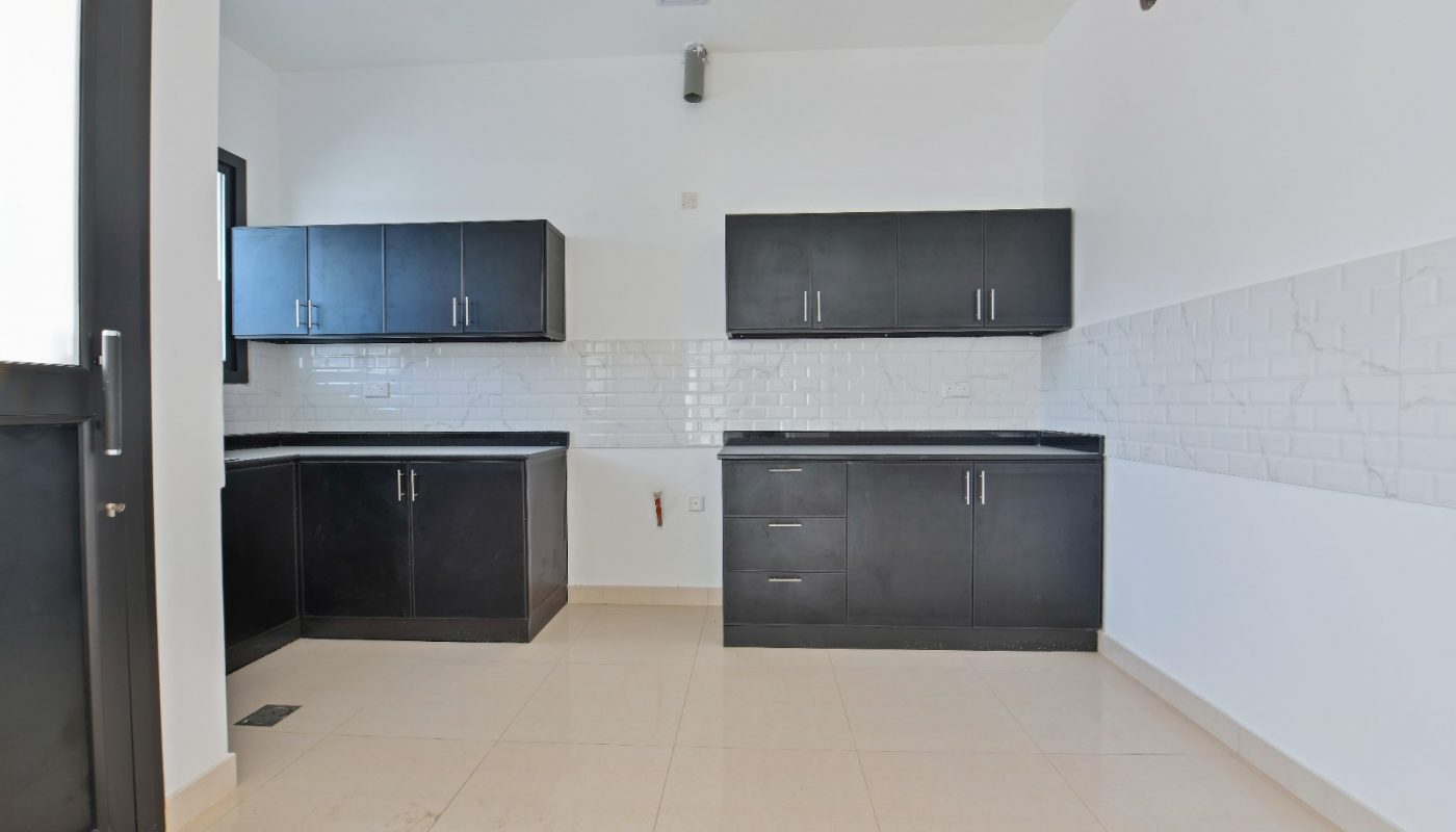Modern kitchen with black cabinets, white tiled backsplash, beige floor tiles, and white walls, featuring no appliances or visible decorations.