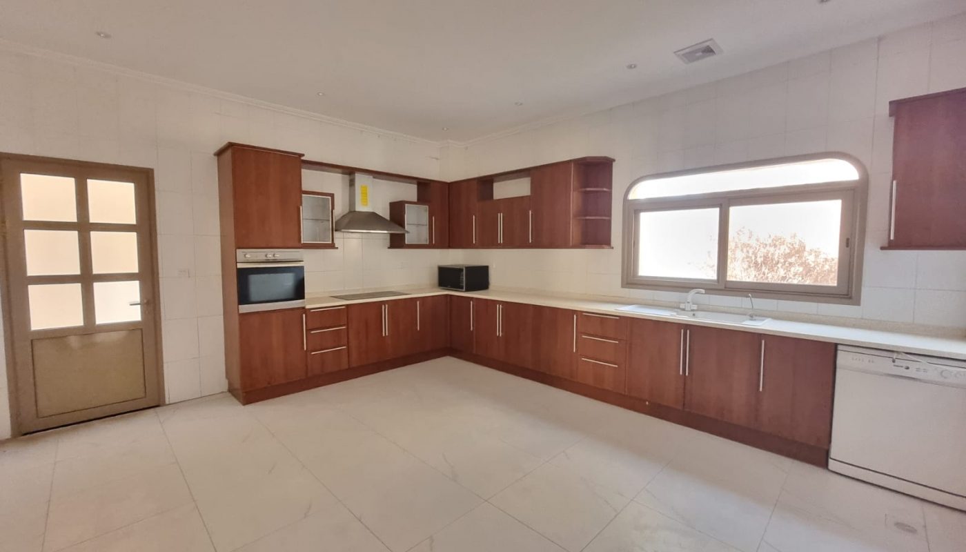 Spacious kitchen with wooden cabinets, white countertops, built-in oven, microwave, dishwasher, and a large window letting in natural light.