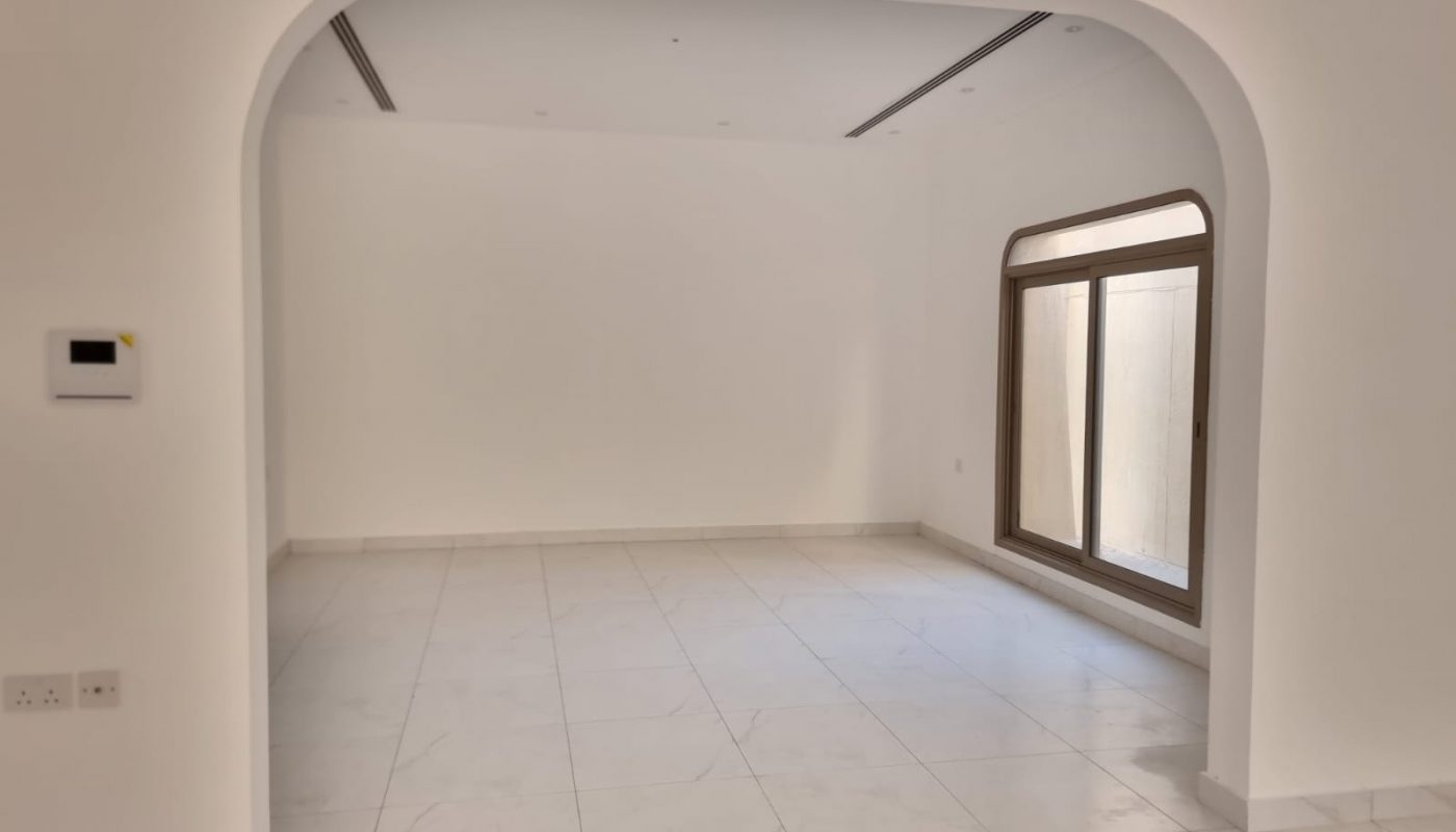 Empty white room with tiled floor, large window with wooden frame on the right, and an arched entryway in the foreground.