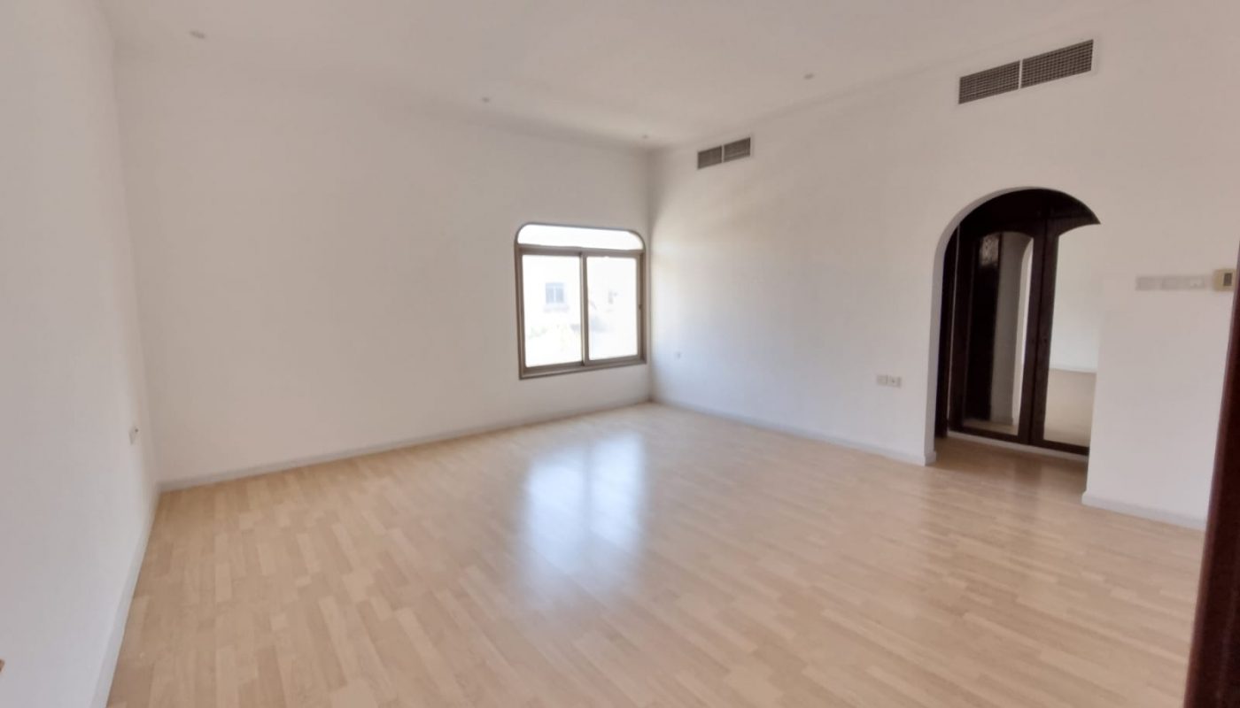 Empty room with light wood flooring, white walls, a large window, an arched doorway, and ceiling air vents.