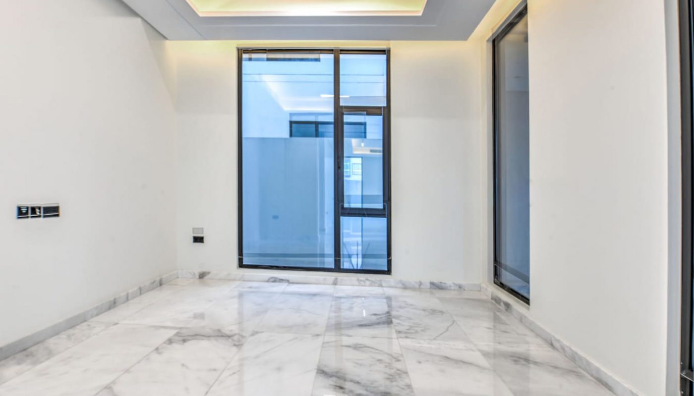 A modern, empty room with marble flooring, white walls, large ceiling lights, and floor-to-ceiling windows.