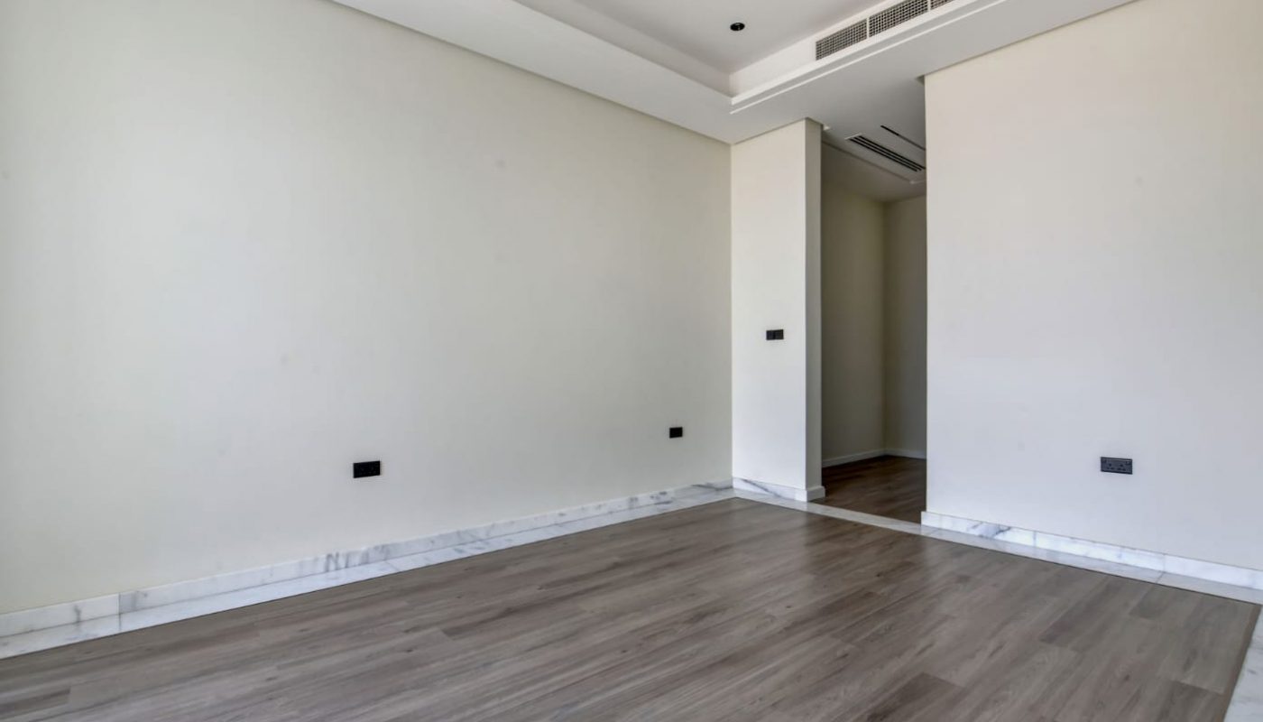 Empty room with light-colored walls, recessed ceiling lights, wood flooring, and a partially open doorway leading to another area.