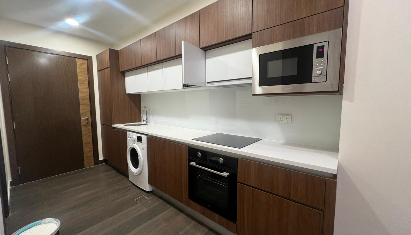Modern kitchen with brown cabinets, white countertop, washing machine, oven, electric cooktop, and microwave; one cabinet door is open.
