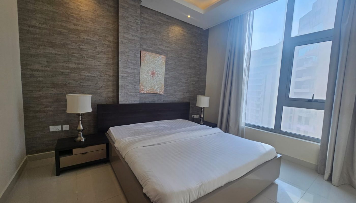 Modern bedroom with a double bed, two bedside tables with lamps, a large window with curtains, and a textured accent wall with artwork above the bed.