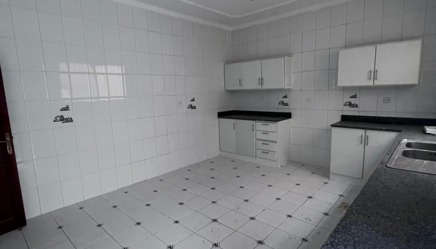 Empty tiled kitchen with white cabinets, granite countertops, ceiling fan, and some dirt on the floor. No appliances or furniture present.