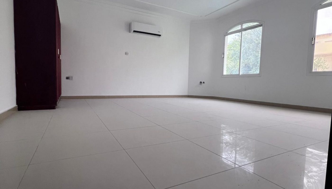 Empty room with white tiled floor, white walls, ceiling fan, wall-mounted air conditioner, two windows, and a dark-colored wardrobe in the corner.