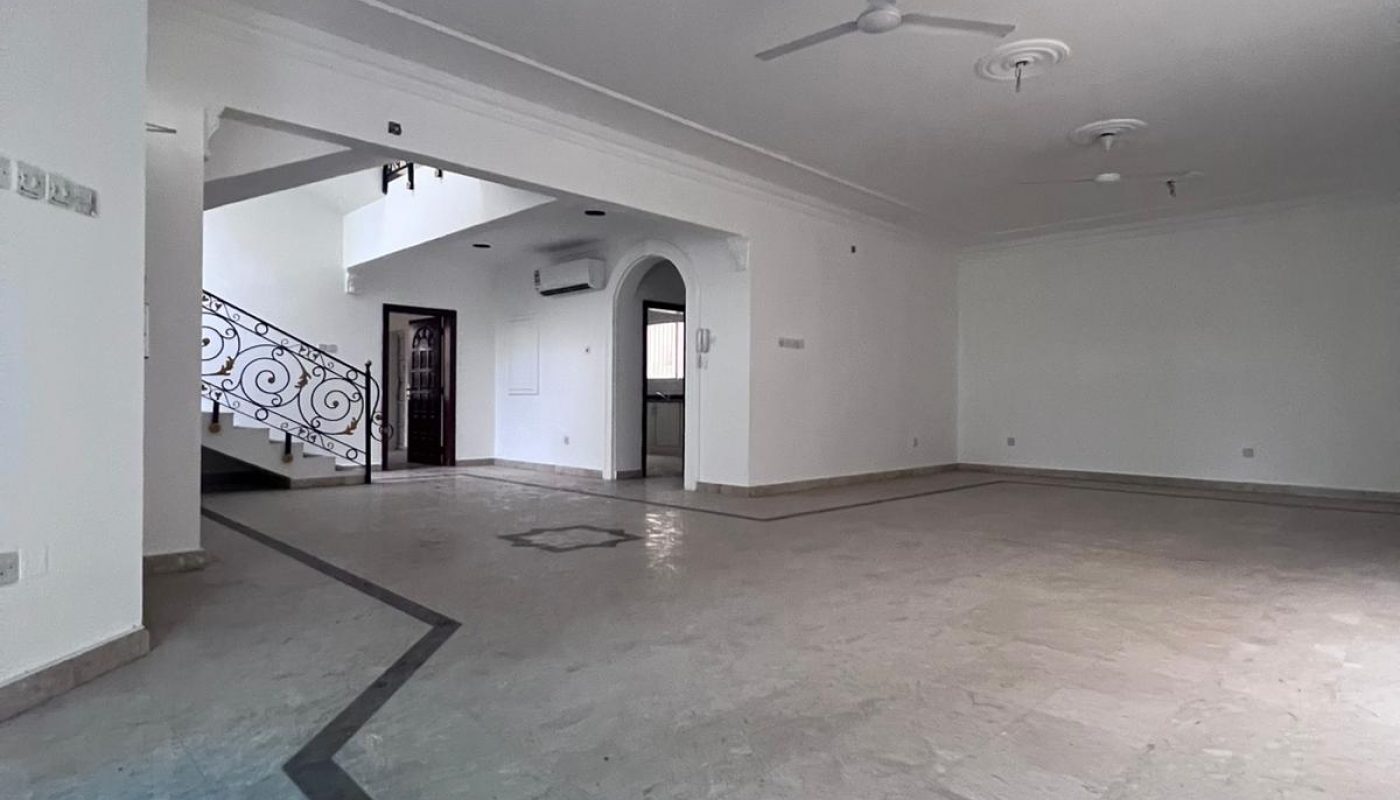 Spacious empty room with marble floor, white walls, two ceiling fans, and a staircase with decorative railing leading to an upper level.