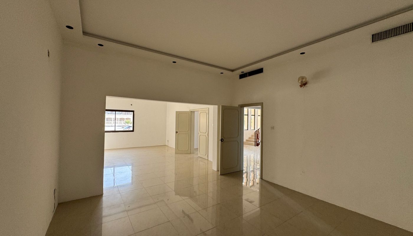 Empty, unfurnished room with white walls, beige tiled floor, an open door, a window, and recessed ceiling lights. Natural light enters from the window and open doorway.