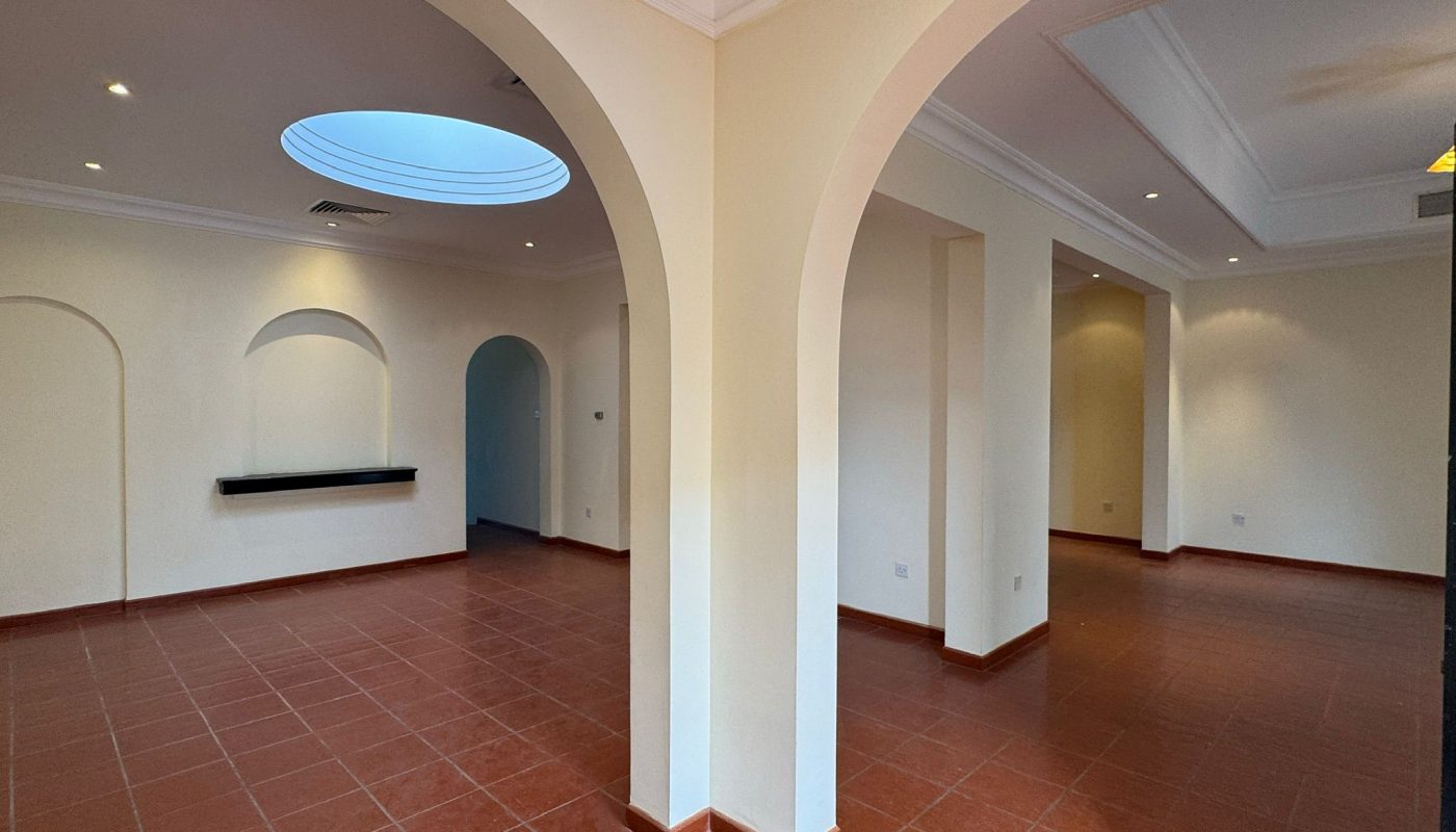 Spacious empty room with terracotta tile floor, white walls, arched doorways, recessed lighting, and a circular skylight in the ceiling.
