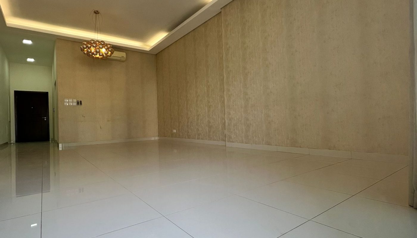 Empty room with large white tiled floor, beige walls, recessed ceiling lights, and two modern chandeliers hanging from the ceiling.