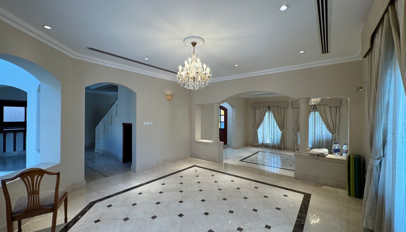 Spacious, unfurnished living room with marble floors, chandelier, large windows with curtains, a single wooden chair, and some items on the floor by the window.