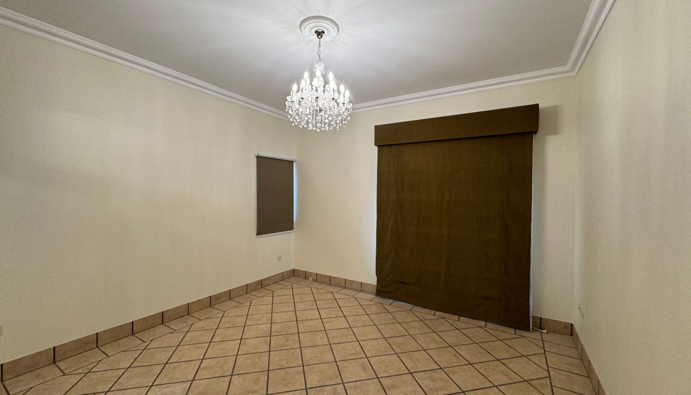 Empty room with cream walls, tile flooring, a chandelier, a small window with a brown shade, and a large covered opening on one wall.