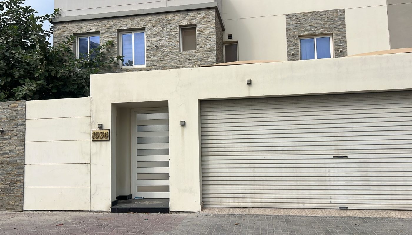 Modern house with a stone and cream-colored facade, featuring a metal gate, a garage door, and two rectangular windows above.