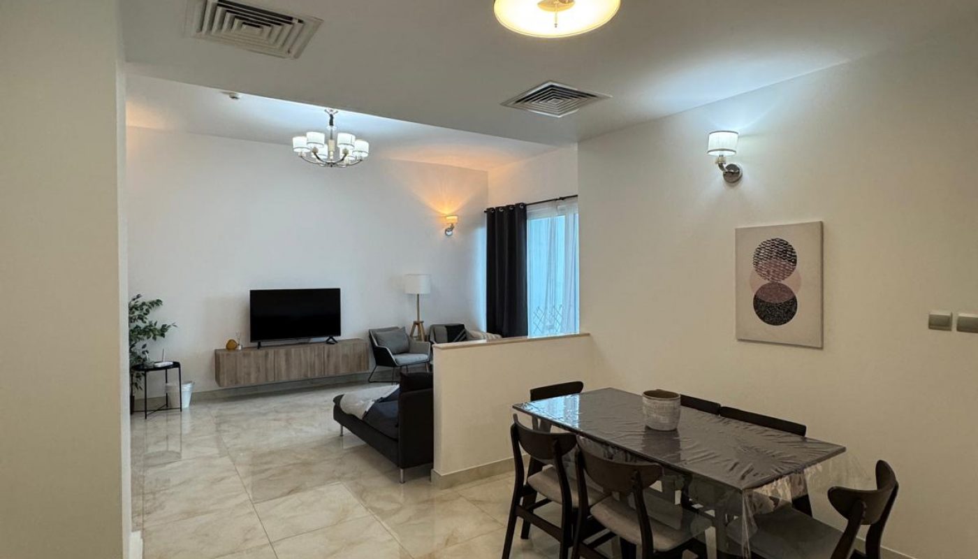 Modern open-plan living and dining area with tiled flooring, a dining table for six, a sofa facing a TV, wall art, and contemporary lighting fixtures.