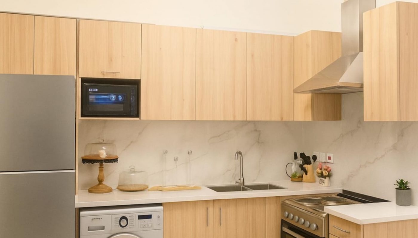 Modern kitchen with light wood cabinets, stainless steel refrigerator, oven, washing machine, microwave, marble backsplash, and a round ceiling light fixture.