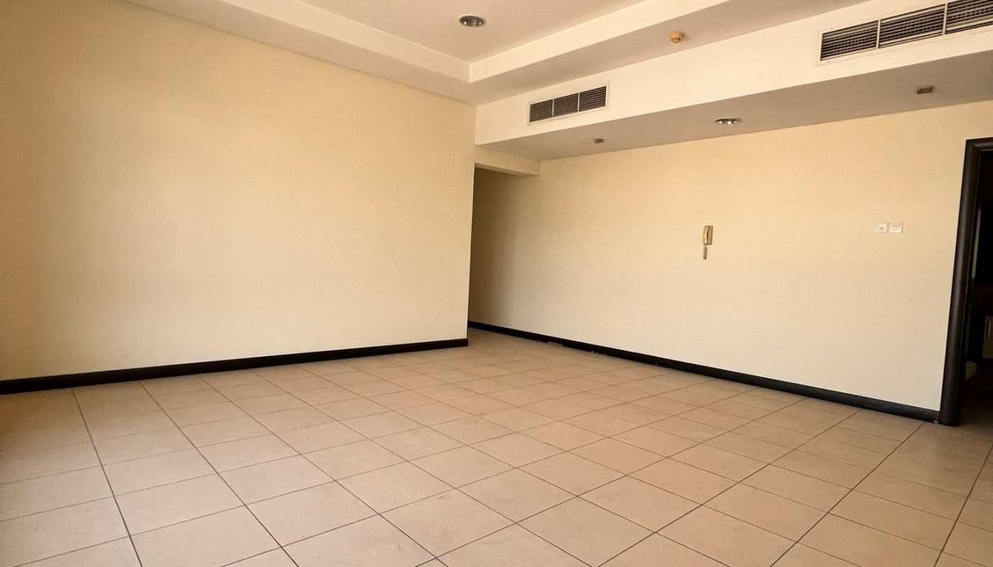 Empty room with beige tiled floor, cream-colored walls, recessed ceiling lights, ceiling fan, and air vents, viewed from a corner.