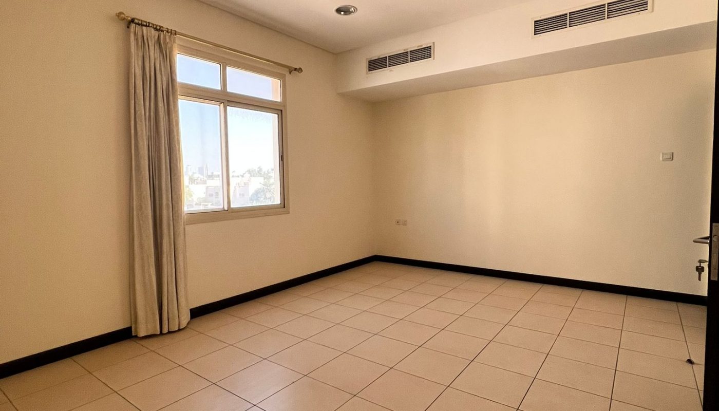 Empty room with beige tiled floor, cream walls, a window with beige curtains, ceiling lights, air vents, and a partially open door.