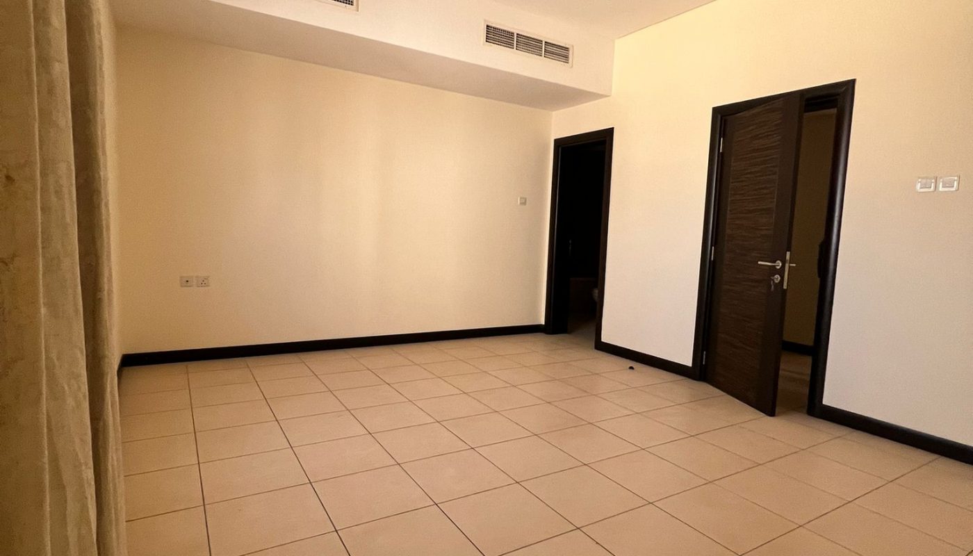 Empty room with beige tiled floor, cream-colored walls, two dark doorways, air conditioning vents on the ceiling, and curtains partially visible on the left side.