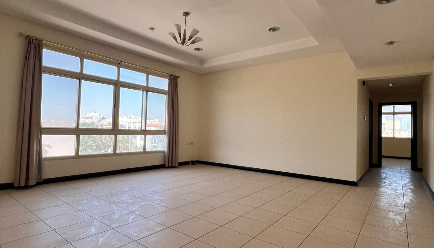 Spacious, empty room with tiled floor, large windows with curtains, recessed ceiling lights, and a modern ceiling fixture. Natural light fills the space.