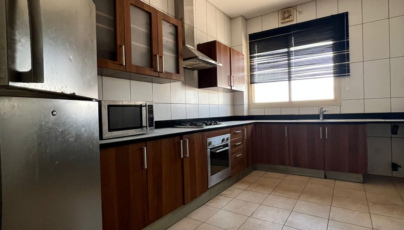 Modern kitchen with stainless steel refrigerator, built-in oven, microwave, dark wood cabinets, tiled floor, and a window with black blinds.