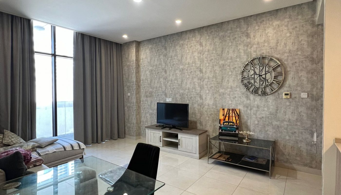 Modern living room with tiled floor, glass dining table and chairs, TV on a stand, wall clock, and large window with floor-to-ceiling curtains.