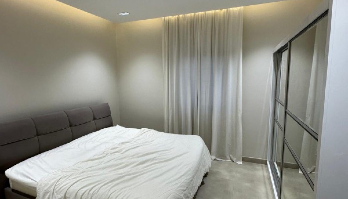 A modern bedroom with a double bed, white bedding, light-colored tile floor, floor-to-ceiling curtains, and a mirrored sliding closet.