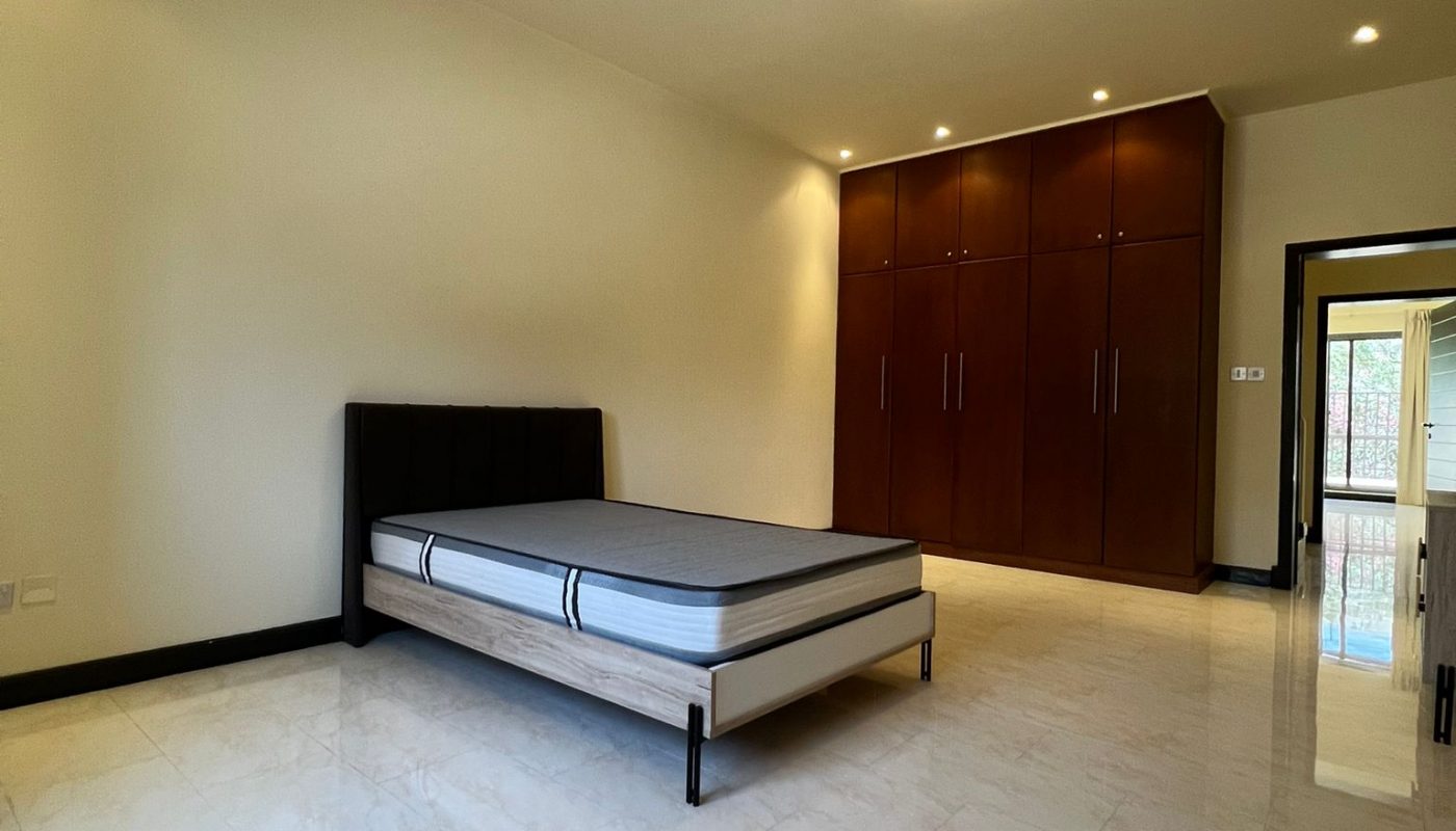 Spacious bedroom with a single bed frame and mattress, tiled floor, built-in wooden wardrobes, and bright overhead lighting.