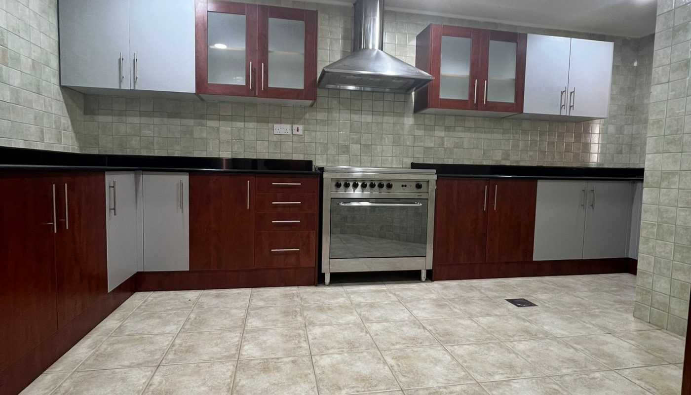 Modern kitchen with tiled floor, stainless steel stove and hood, upper and lower cabinets in white and wood finish, and tiled backsplash.