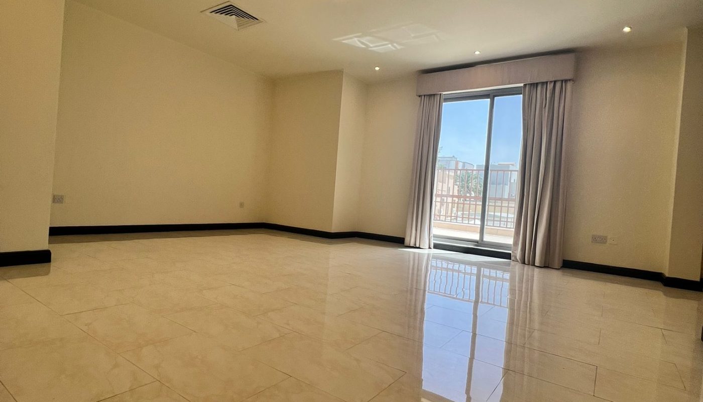 Spacious, empty room with glossy tiled floor, beige walls, ceiling lights, and large sliding glass doors leading to a balcony with a view outside.