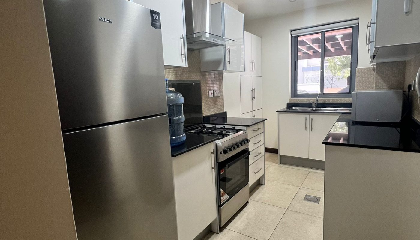 Modern kitchen with stainless steel refrigerator, stove, and white cabinets; water dispenser beside fridge; window at end of room; tiled floor and countertops.
