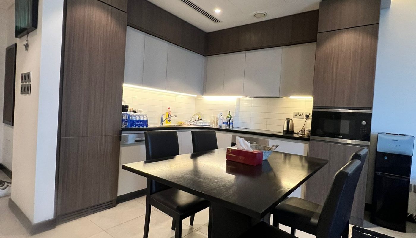 Modern kitchen with dark wood cabinets, built-in appliances, a countertop with various items, and a black dining table with four chairs in the center.