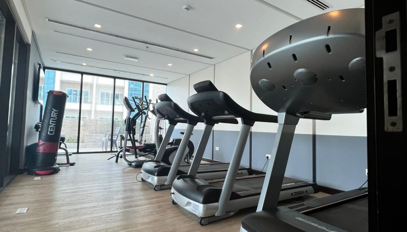 Modern gym room with treadmills, elliptical machines, and a punching bag on a wooden floor, viewed from the entrance.