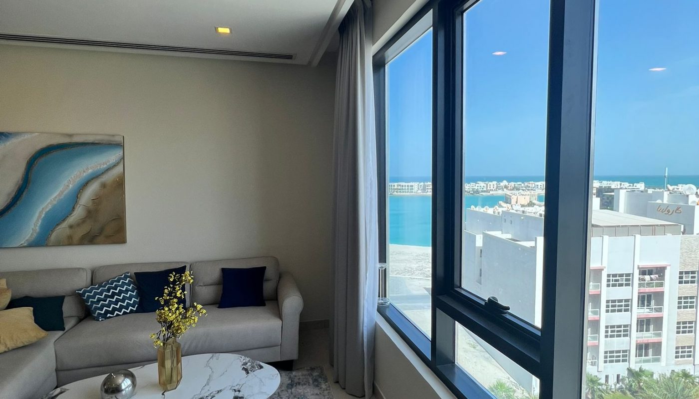 A modern living room with a beige sofa, marble coffee table, large windows with city and water views, and neutral décor.