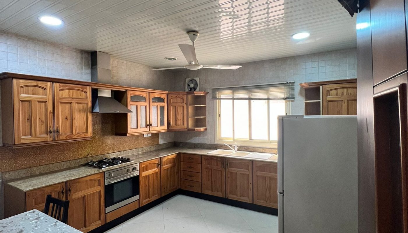 A spacious kitchen with light wood cabinets, a gas stove, refrigerator, and a dining table with a patterned tablecloth.
